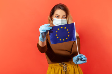 Woman in hygienic face mask and gloves showing European Union flag, concept of coronavirus pandemic threat in Europe, closed borders, visa abolition and travel restriction. indoor studio shot isolated