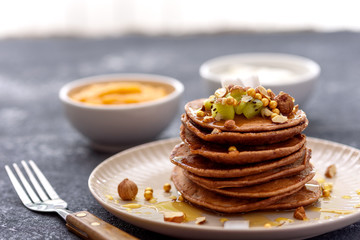 chocolate pancakes in beige plate with fork, mango jam and sour cream on gray background