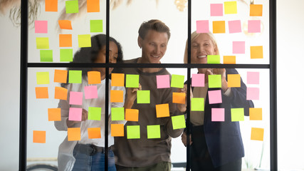 Diverse employees team writing tasks or ideas on colorful sticky papers, making post it notes on...