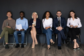 Group portrait smiling business people sitting on chairs in row, looking at camera, successful candidates holding resume documents, waiting for job interview in queue, human resources concept