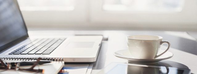 Workplace, laptop computer, coffee cup and digital notebook at office desk, panoramic banner....