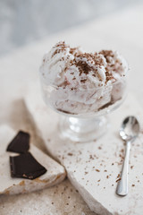 Vanilla ice cream sprinkled with chocolate chips in a transparent bowl on a light stone background