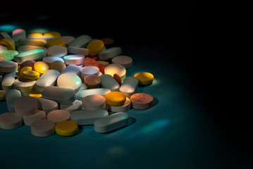 White, yellow, red, orange and blue pills on a cardboard background. Medication on a dark background with contrasting dramatic light.