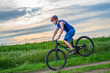 A cyclist in a helmet standing on the front wheel of a bicycle.