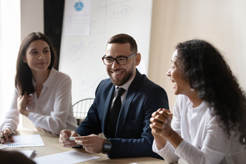 Confident businessman leader mentor wearing glasses with diverse colleagues laughing at funny joke at corporate meeting, friendly business team having fun at briefing, good staff relationship