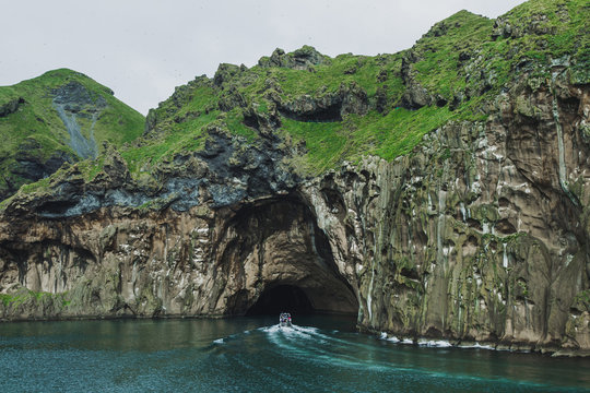 Rocky coast of Vestmannaeyjar island, Iceland with huge water cave. Weathering and erosion mountain surface. Tourist boat in adventure trip.