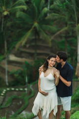 Young latin pregnant woman with husband with amazing view of Ubud rice terraces. Pregnant couple happy together.