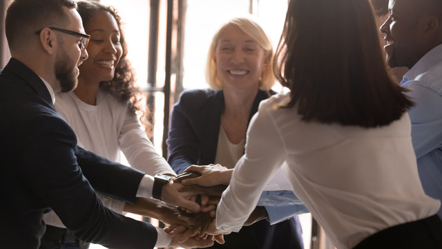 Smiling diverse colleagues joining stacking hands at workshop, engaged in team building, excited business team celebrating success, good teamwork result, business achievement at corporate meeting