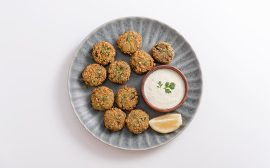 Homemade falafel with Tzatziki sauce in a wooden bouwl served in a plate. With Cilantro and parsley. White background.