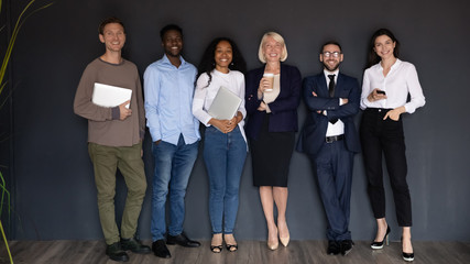 Fototapeta premium Smiling diverse business people standing in row on black wall background, successful happy employees team with leader boss looking at camera, staff posing for corporate portrait in office