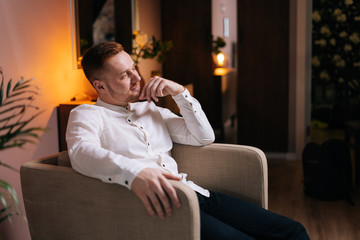Fototapeta premium Calm happy young man sitting in soft armchair at home in cozy living room