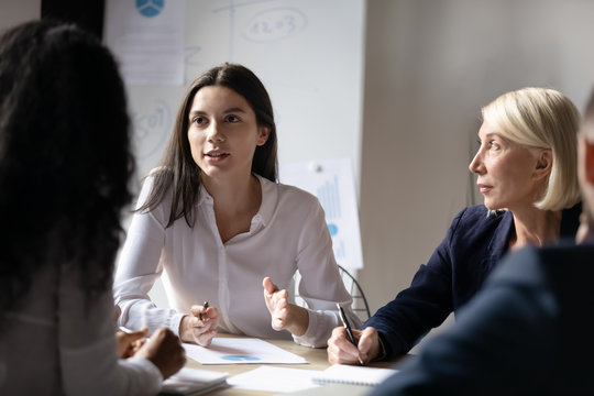 Confident young businesswoman speaking at corporate meeting, female intern sharing startup ideas, discussing project strategy with colleagues at briefing, group business partners negotiation