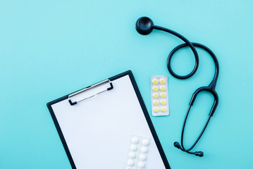 Black modern stethoscope, tablets and blank medical form on light blue background.