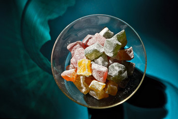 Lots of sweets in a glass jar on a blue background. Candy with white icing sugar close up.