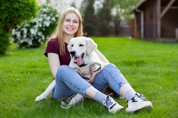 girl with a puppy of a retriever sits on a green grass in the spring on the street, a woman plays with a dog