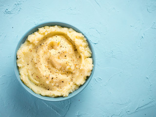 Mashed potatoes with peppers in blue bowl on blue concrete background. Top view or flat lay. Copy space.