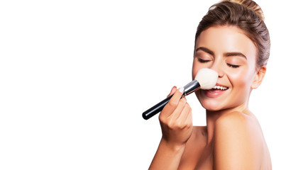 Close up of a brunette cute woman face with fresh clean flawless skin. She apply mascara on her face with a brush. Studio beauty portrait on white background