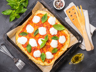 Top view of homemade cauliflower pizza crust with mozarella and fresh basil in dripping pan on black concrete background.