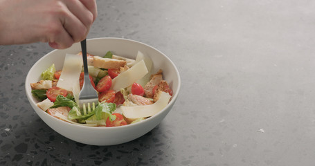 Man hand pick caesar salad with fork from white bowl on concrete background