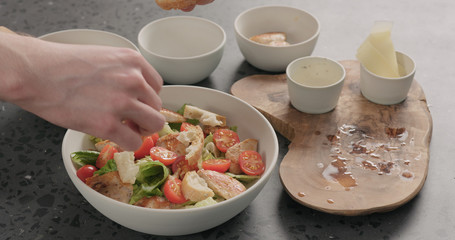 Man hand add croutons on caesar salad in white ceramic bowl on concrete countertop