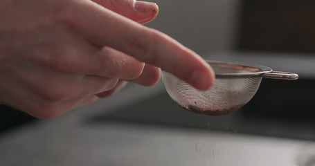 man hand sprinkle cocoa powder from sieve