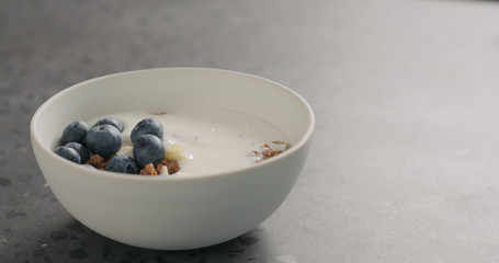 ripe blueberries and chocolate granola in white bowl on terrazzo surface