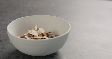chocolate granola fall into white bowl on terrazzo surface