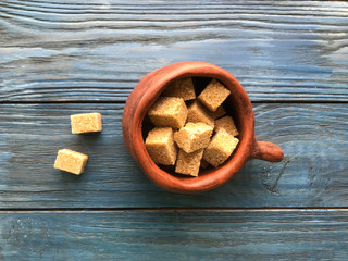 pieces of brown sugar in a ceramic mug on a wooden background