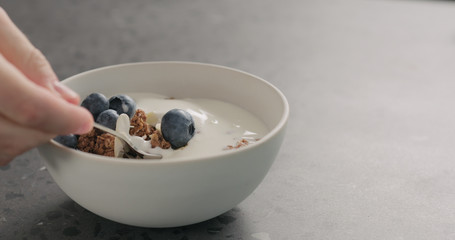 man hand tastes chocolate granola with almond flakes and blueberries in white bowl on concrete surface