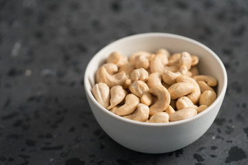 Dry cashew nuts in white bowl on concrete background with copy space