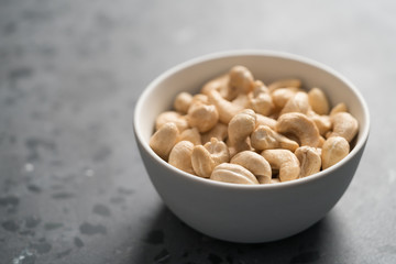 Dry cashew nuts in white bowl on concrete background with copy space
