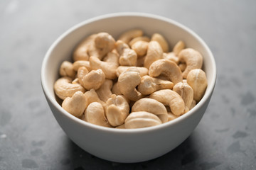 Dry cashew nuts in white bowl on concrete background closeup