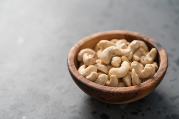 Dry cashew nuts in wood olive bowl on concrete background with copy space