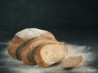 Sliced homemade sourdough rye bread with rye flour on black textured background. Copy space. Low key