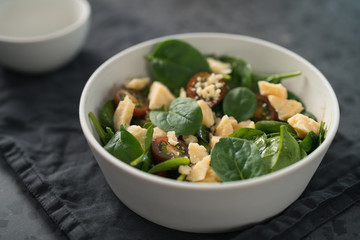 Salad with spinach, kumato tomatoes and cheese in white bowl on linen napkin