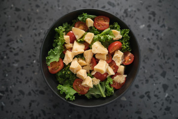 Salad with cherry tomatoes, kale and cheese in black bowl on concrete background