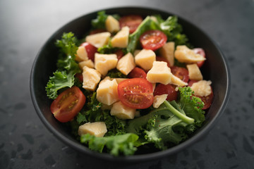 Salad with cherry tomatoes, kale and cheese in black bowl on concrete background