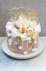 Light brown and golden colored birhtday cake with macaroons, coins, meringue and lollipops.