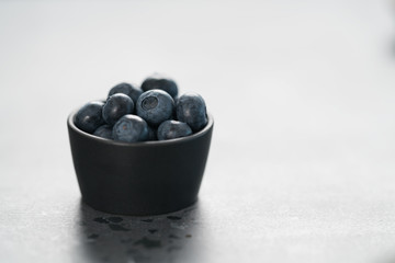 Fresh ripe blueberries in small black bowl on concrete background with copy space