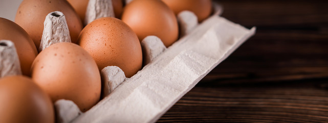 Banner detail close-up of chicken eggs in egg box on the old brown wooden background.