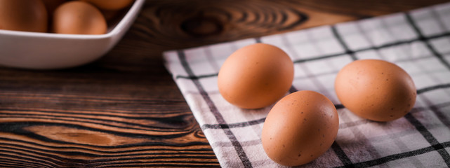 Banner detail close-up of chicken eggs on the old brown wooden background.