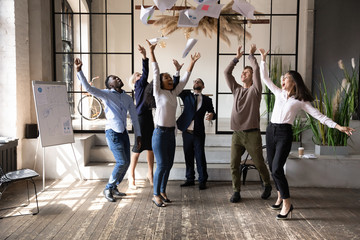 Excited diverse business people throwing papers, celebrating sharing teamwork success, laughing and...
