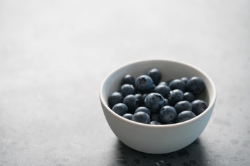 Fresh ripe blueberries in white bowl on concrete background with copy space