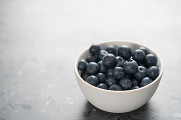 Fresh ripe blueberries in white bowl on concrete background with copy space