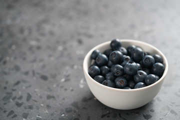 Fresh ripe blueberries in white bowl on concrete background with copy space