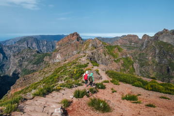 Mother with teenager son trekking the famous mountain footpath from Pico do Arieiro to Pico Ruivo on the Portuguese Madeira island. Around the world traveling with kids concept image. - obrazy, fototapety, plakaty