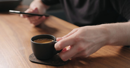 unrecognizable man sitting at the walnut table with smartphone and drink fresh espresso