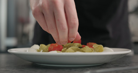 Obraz na płótnie Canvas man put cherry tomatoes on pesto fettuccine with mozzarella in pasta bowl on concrete countertop