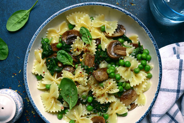 Pasta farfalle with mushrooms, spinach and green pea. Top view with copy space.