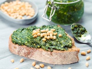 Close up view of whole grain rye bread with fresh basil pesto sauce on gray wooden table. Copy space.